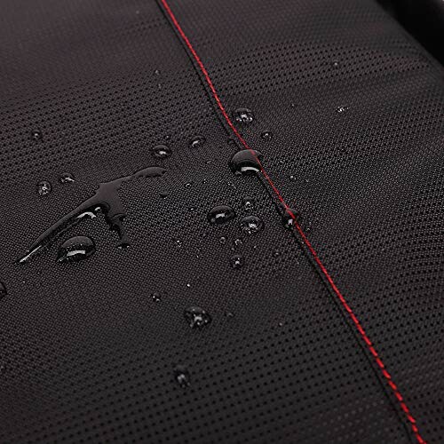 Close-up of water droplets on black waterproof fabric with red stitching.